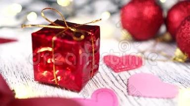 红色礼盒搭配金结和粉心特写.. 明亮的装饰球和丝带。 圣诞树亮灯亮灯